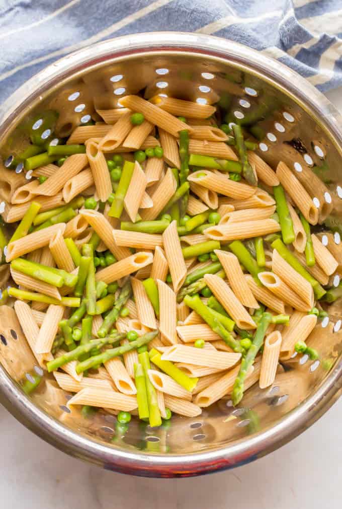 Cooked pasta and asparagus and peas in a silver colander