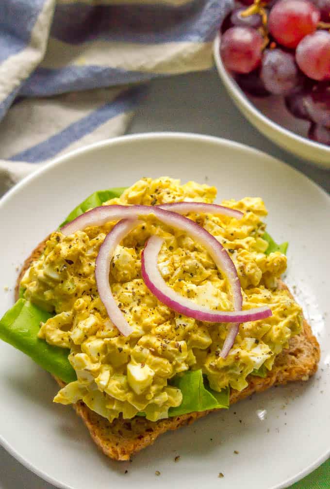 Curried egg salad being served open-faced on a piece of toast with lettuce and red onion rings