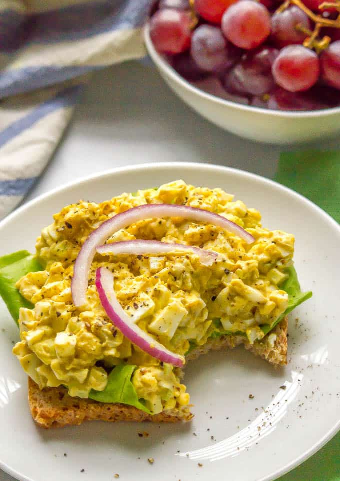Curried egg salad being served open-faced on a piece of toast with lettuce and red onion rings with a bite taken out