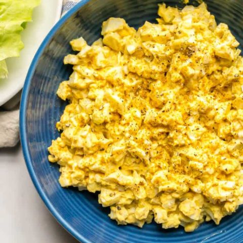 Overhead shot of curried egg salad in a blue bowl with a blue striped towel nearby