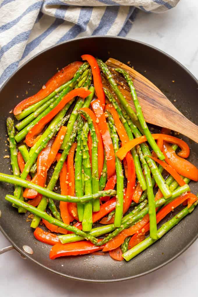 Sesame asparagus and red peppers in a saute pan with a wooden spoon