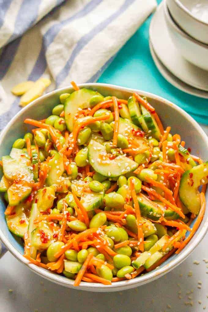 A blue tinted bowl with a veggie salad of carrots, cucumber and edamame in a soy style dressing with sesame seeds on top.