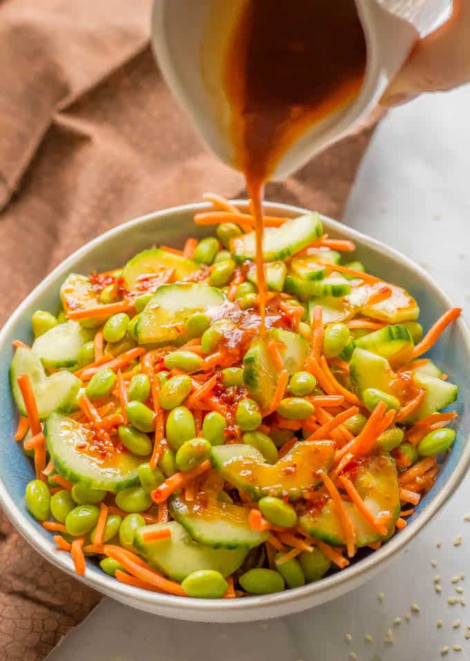 Soy ginger dressing being poured over edamame, carrot and cucumber salad