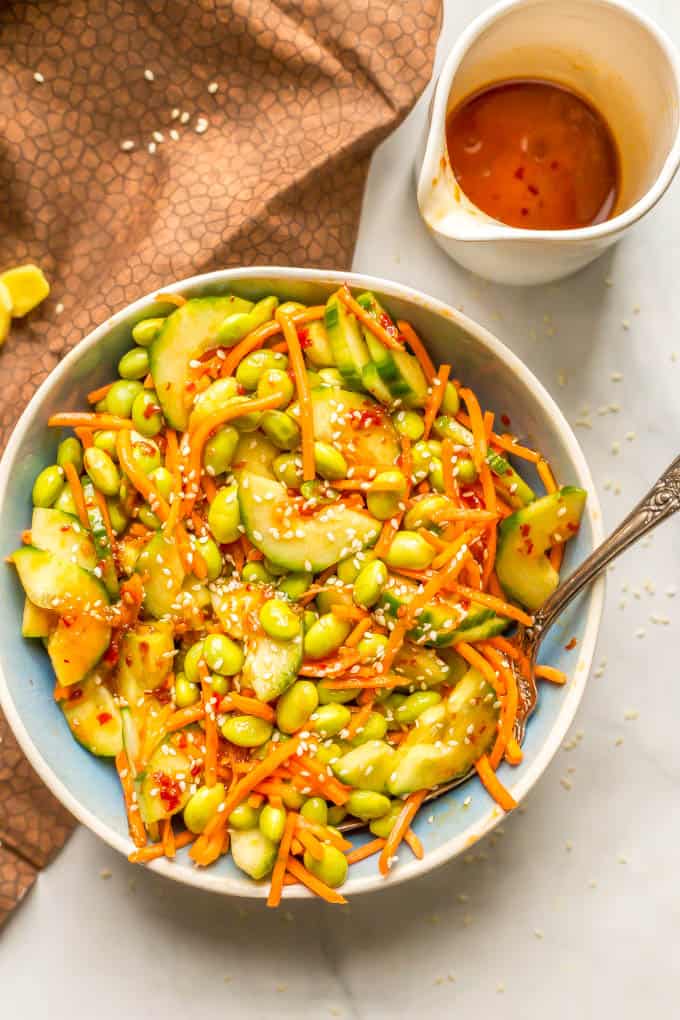 Overhead shot of edamame, carrot and cucumber salad in a blue bowl with soy ginger dressing nearby