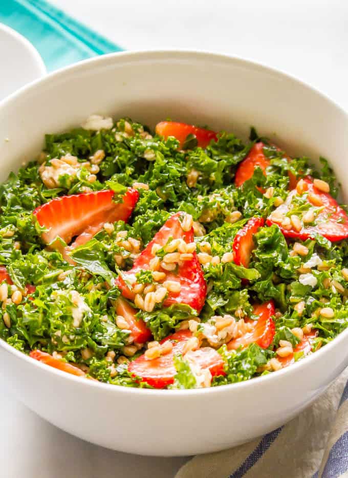 A white bowl full of a kale and farro salad with strawberries and goat cheese.