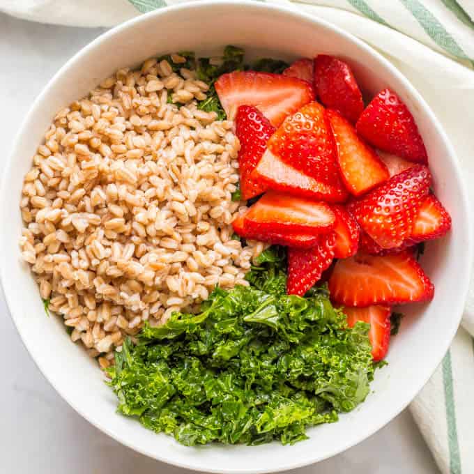 Farro, kale and strawberry salad ingredients separated in a white bowl