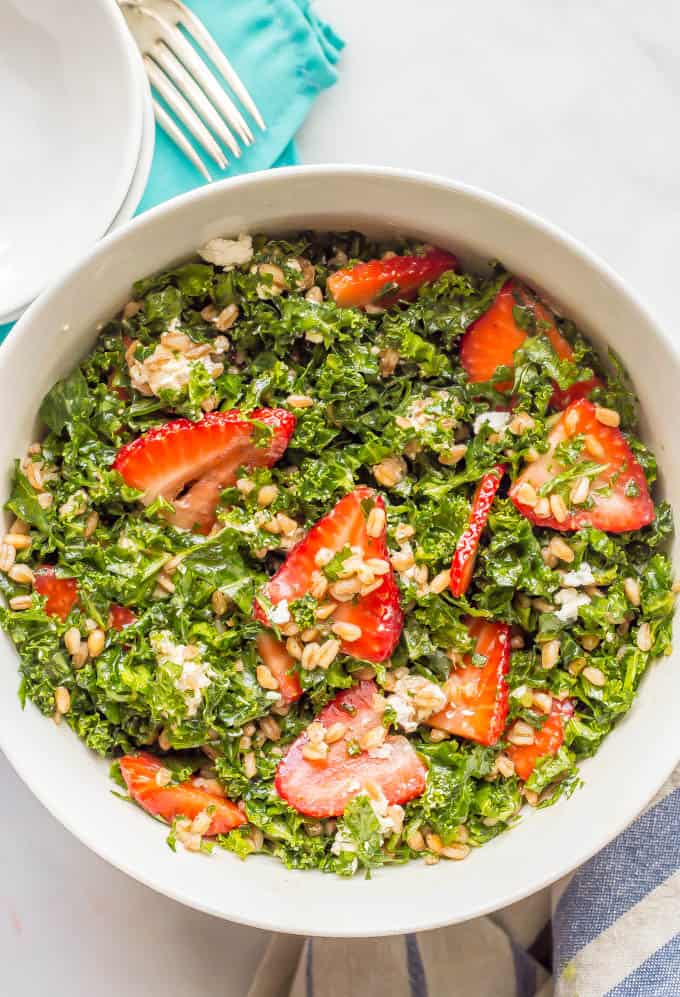 Overhead shot of farro kale and strawberry salad with goat cheese in a white bowl