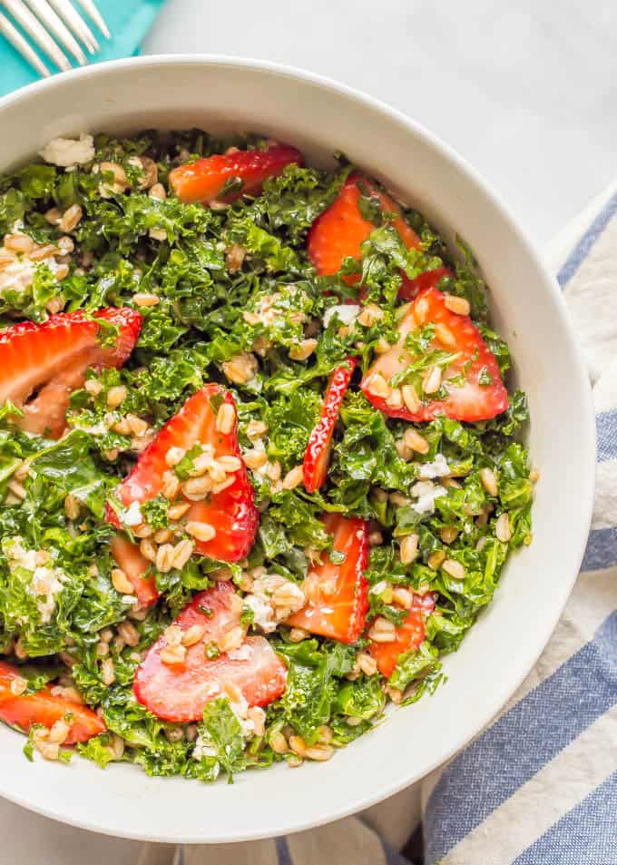 Overhead close-up shot of farro kale and strawberry salad with goat cheese in a white bowl