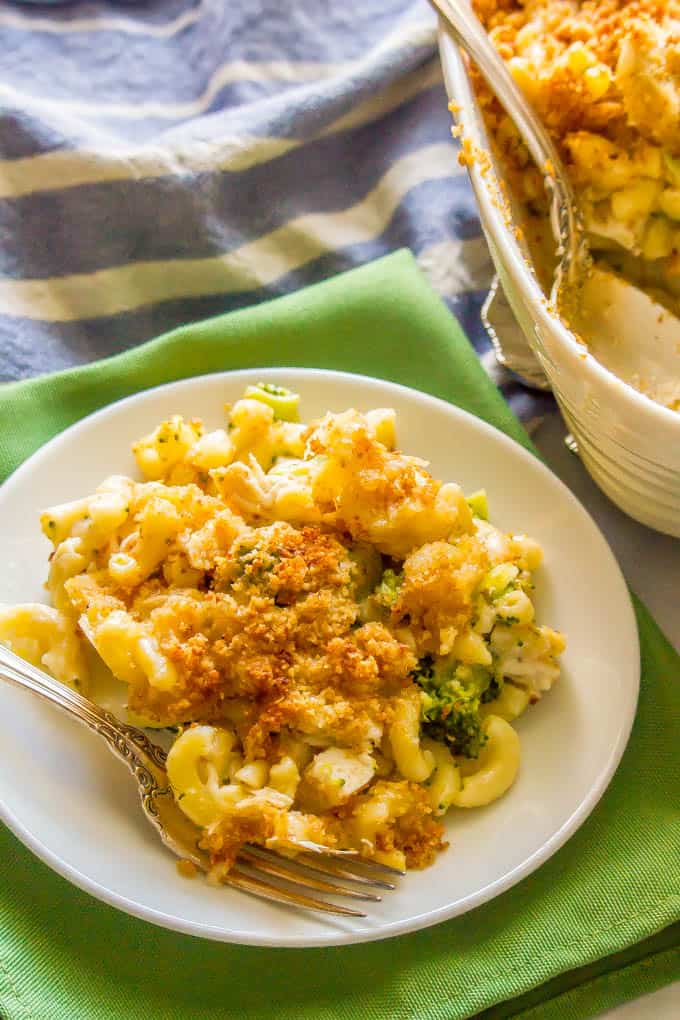 A serving of healthy chicken broccoli mac and cheese being served on a small white plate with a fork on the plate and a green napkin underneath