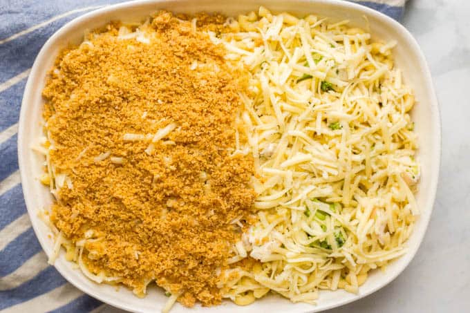 Image of layered healthy chicken broccoli mac and cheese with a buttery breadcrumb topping being added to the casserole dish