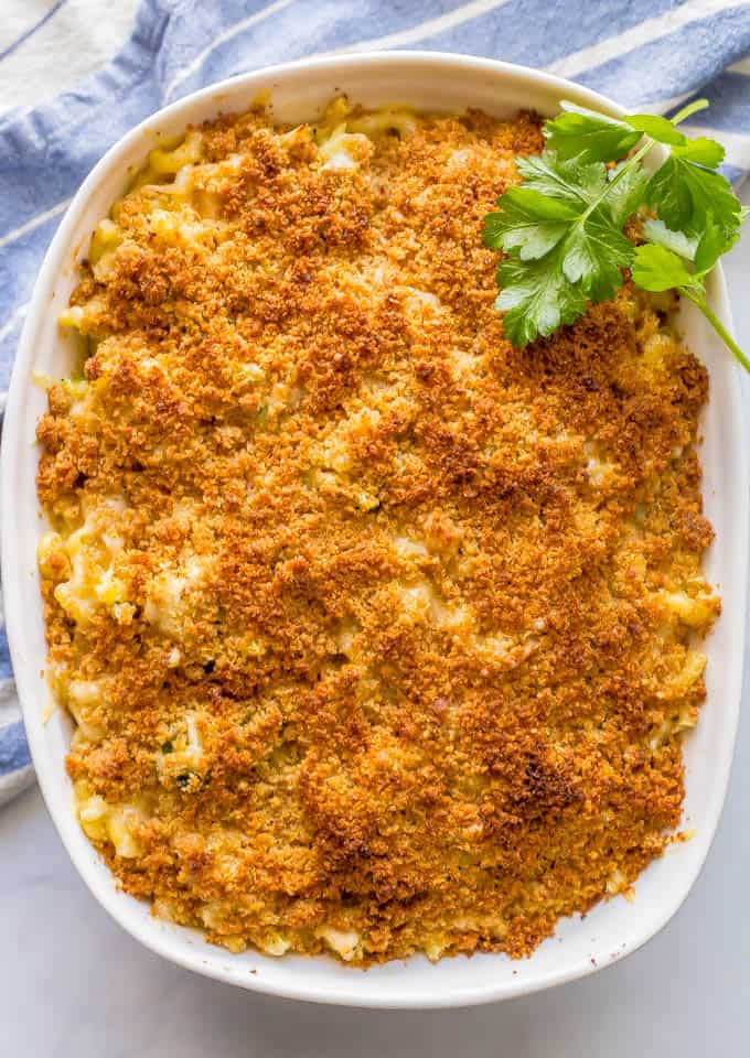 Overhead shot of baked healthy chicken broccoli mac and cheese casserole with a buttery breadcrumb topping and a blue striped towel nearby