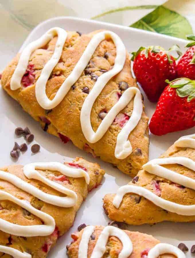 Close up of homemade strawberry scones with mini chocolate chips and a drizzle of a thick icing on top.