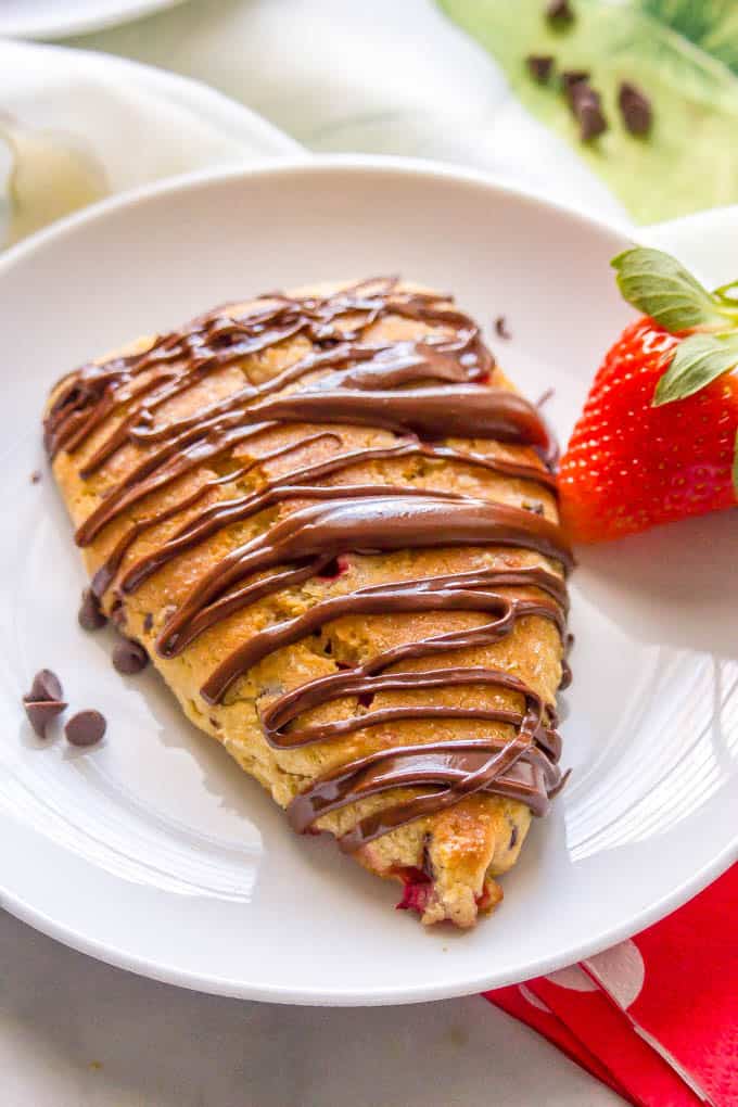 Close-up of a Nutella-drizzled healthy strawberry scone on a white serving plate