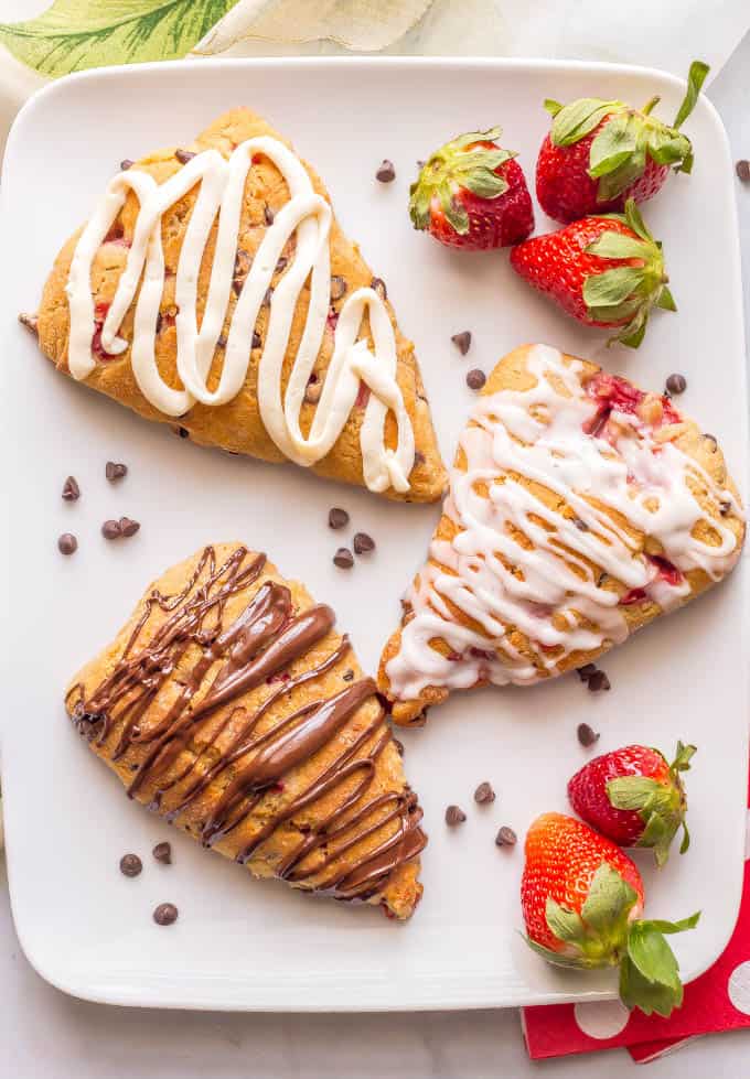 Healthy strawberry scones on a platter with mini chocolate chips, fresh strawberries and a variety of frostings and glazes drizzled on top