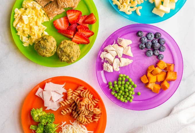 Overhead image of colorful plates with a variety of healthy baby finger foods and toddler finger foods