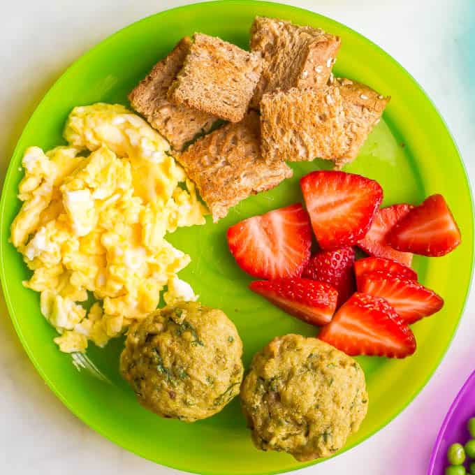 Green kids plate with scrambled eggs, toast pieces, strawberries and mini spinach banana muffins