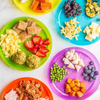 Overhead image of colorful plates with a variety of healthy baby finger foods and toddler finger foods