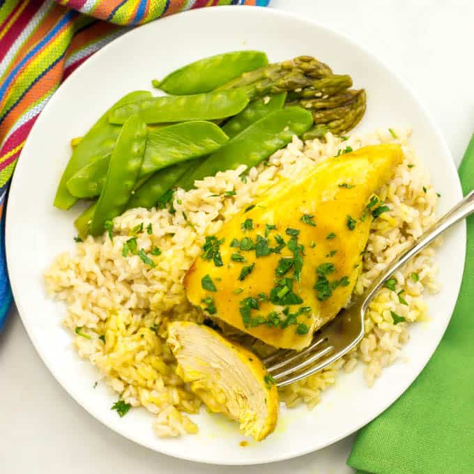 Honey butter chicken served over brown rice with snow peas and asparagus on a white round plate