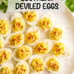 A white round serving platter filled with deviled eggs sprinkled with a little paprika with parsley to the side as garnish and a text overlay on the photo.
