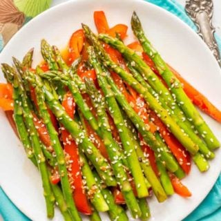 Sesame asparagus and red peppers on a round white plate with napkins in the background