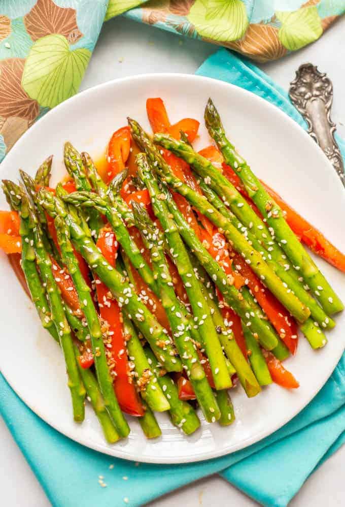 Sesame asparagus and red peppers on a round white plate with napkins in the background