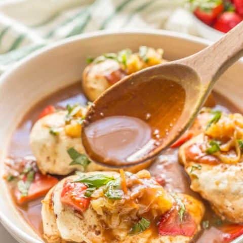 White dish with strawberry balsamic chicken with mozzarella with sauce being spooned over one chicken