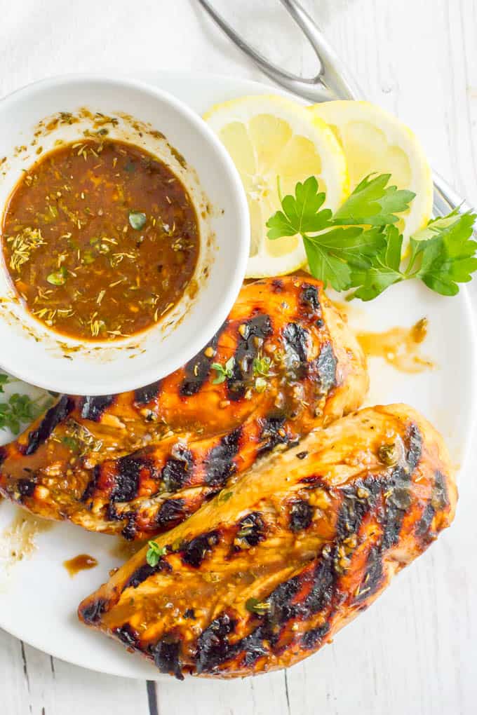 Balsamic herb grilled chicken marinade in a white bowl on a plate with grilled chicken breasts and lemon slices