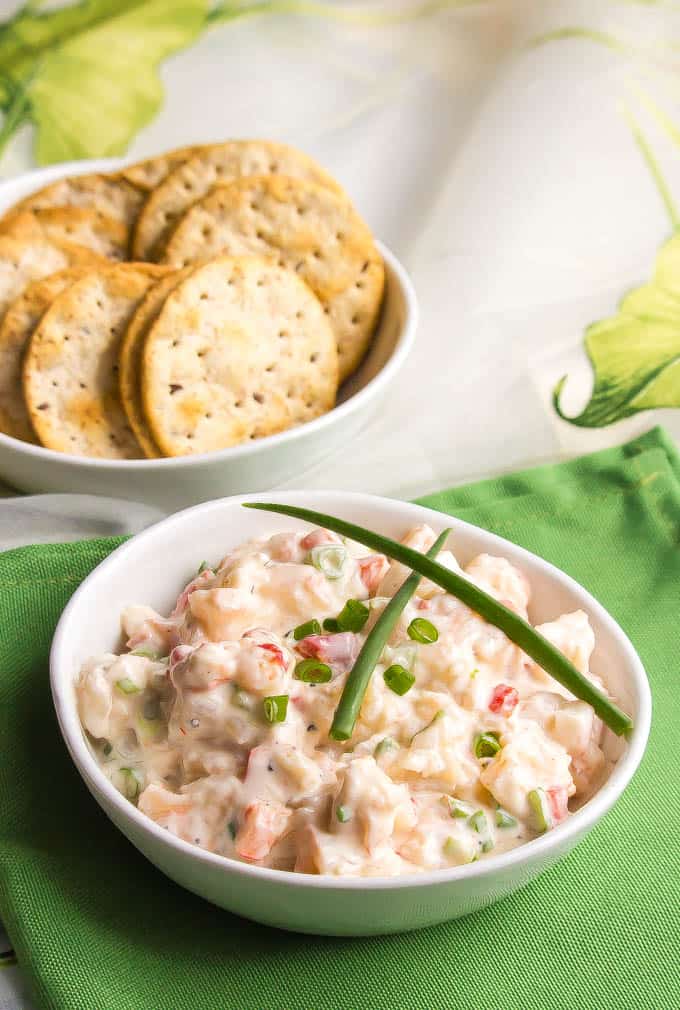 Creamy shrimp salad in a white bowl on a green napkin with a bowl of crackers in the background