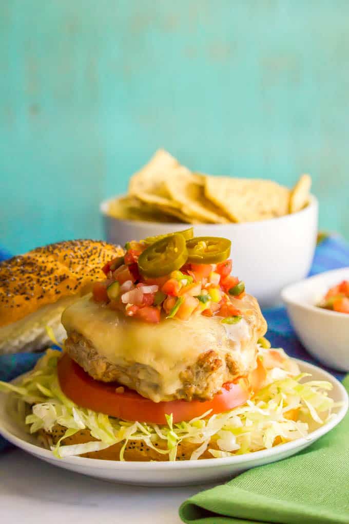 A turkey burger with melty cheese on top served over shredded lettuce and a tomato slice with pico de gallo and pickled jalapenos on top.