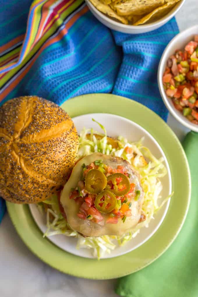 Overhead shot of fiesta turkey burger on a bun on a white plate with toppings and bowls nearby of pico de gallo and tortilla chips