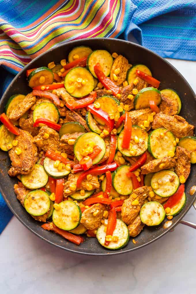 Overhead photo of chicken skillet with zucchini and corn and red peppers cooked in the pan before toppings are added