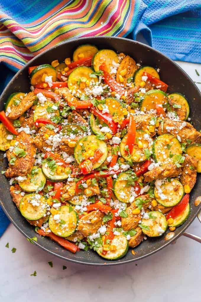A chicken and zucchini mixture with peppers in a large dark skillet with fresh herbs and cheese sprinkled on top.