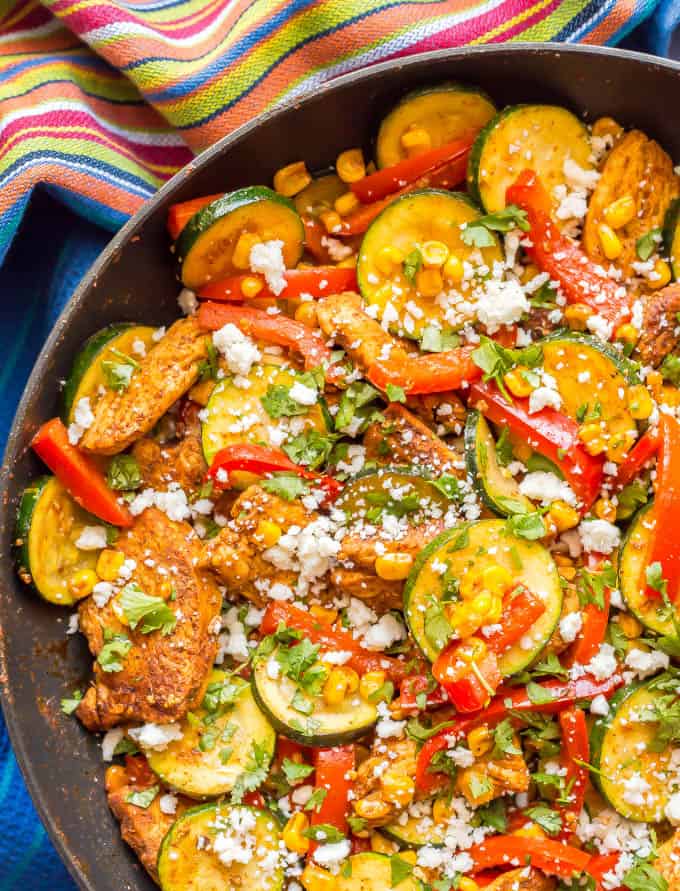 Close-up of healthy chicken and zucchini skillet with corn and peppers in a pan with a striped towel underneath