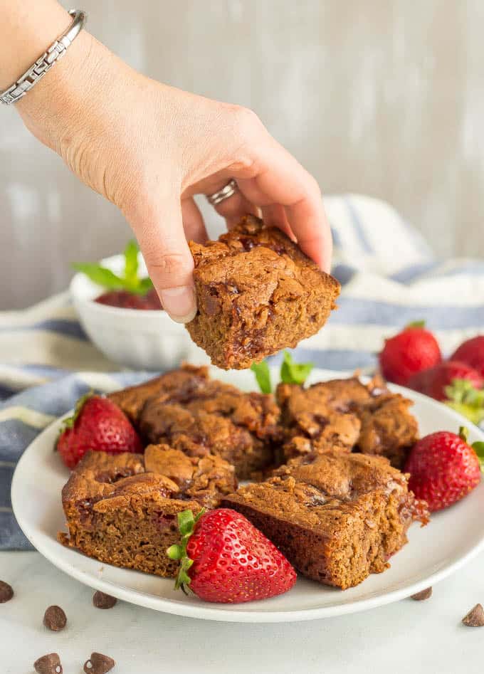 A plate of healthy strawberry brownies with strawberries on the side and one brownie being picked up