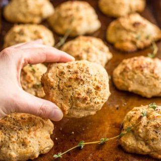 A hand picking up a Parmesan herb drop biscuit from a baking tray