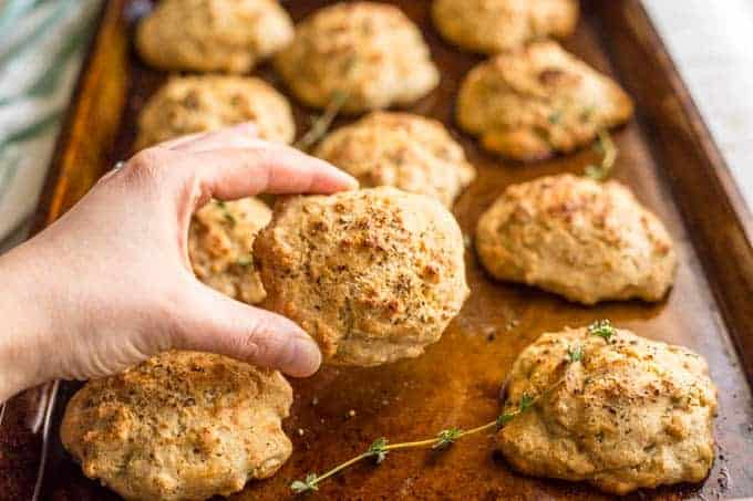 A hand picking up a Parmesan herb drop biscuit from a baking tray