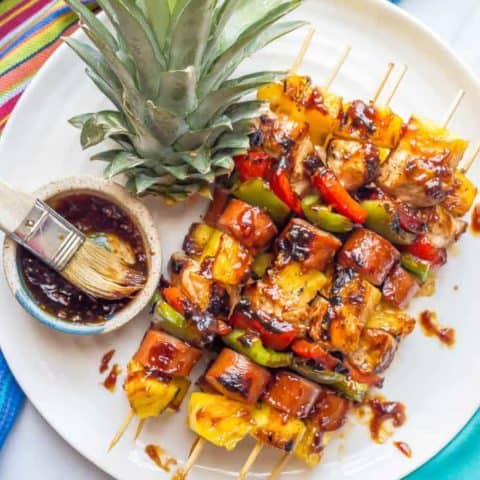 Grilled teriyaki chicken kabobs on a white plate with extra teriyaki sauce on top