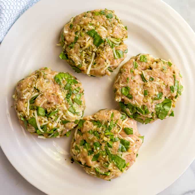 Chicken spinach burger patties on a white plate before being cooked