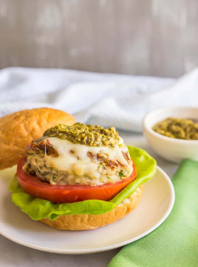 Chicken spinach burger topped with mozzarella cheese and pesto on a bun with lettuce and tomato