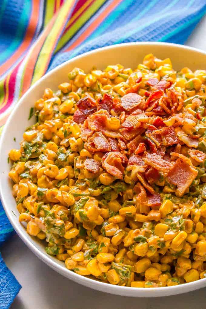A bowl of a corn salad with poblanos and cilantro, topped with cooked, crumbled bacon.