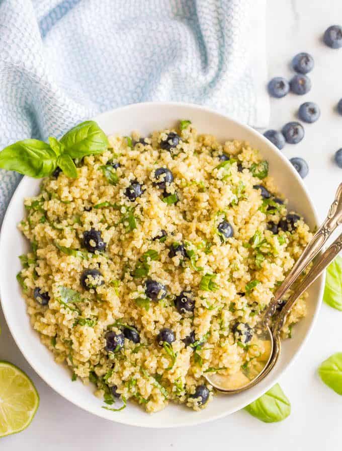 Spoons resting in a low white bowl full of a quinoa salad with blueberries and basil.