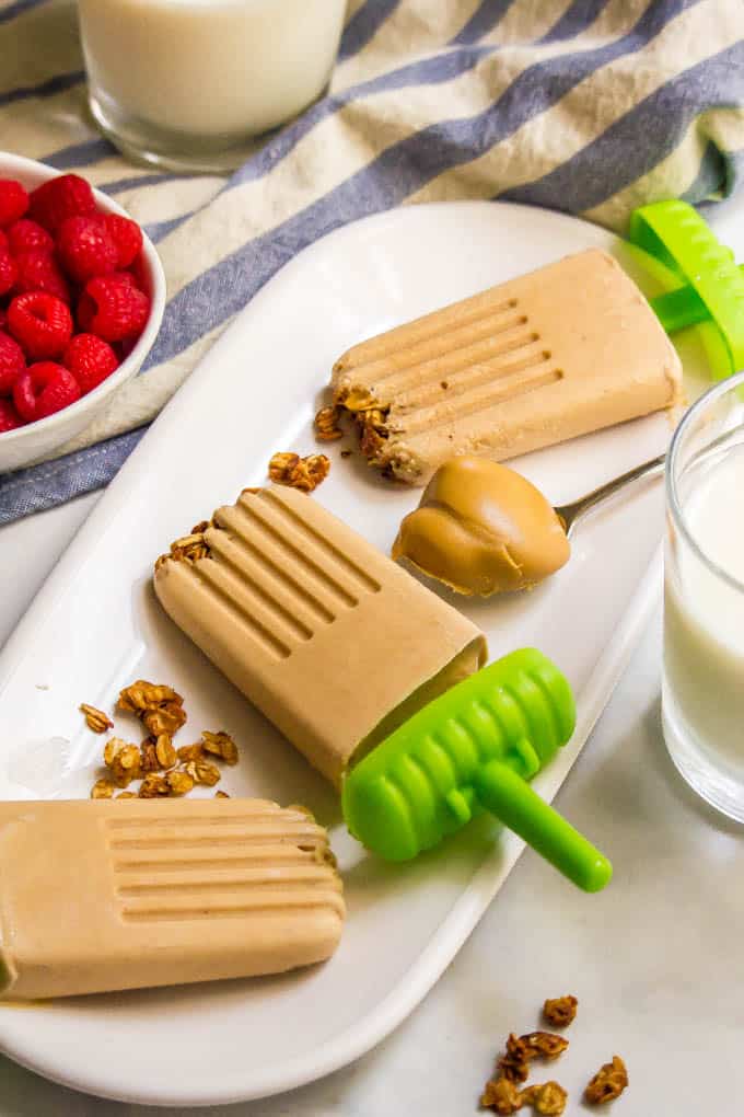 Healthy breakfast popsicles on a plate with granola and a dollop of peanut butter