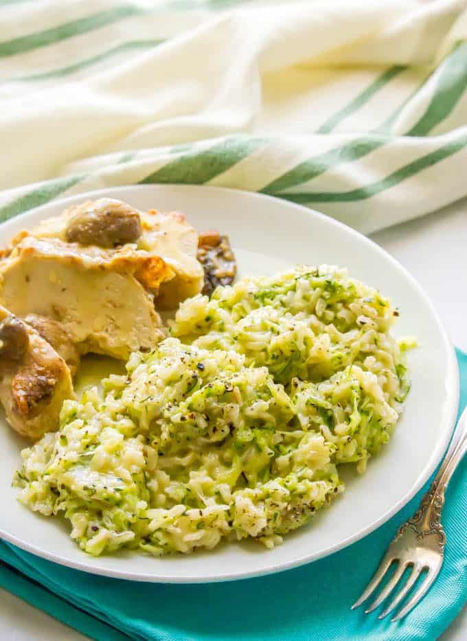 Cheesy zucchini brown rice served on a white plate with chicken