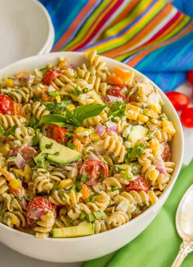 Summer veggie pasta salad in a white bowl with fresh basil on top and colorful napkins nearby