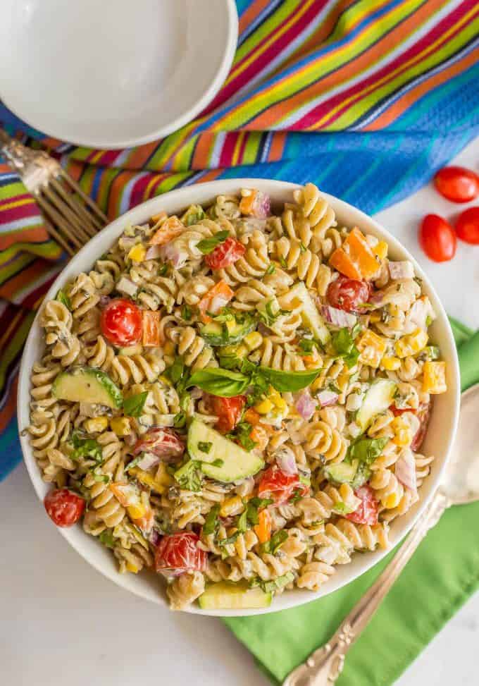 Summer veggie pasta salad in a large white bowl with colorful napkins nearby and a serving spoon