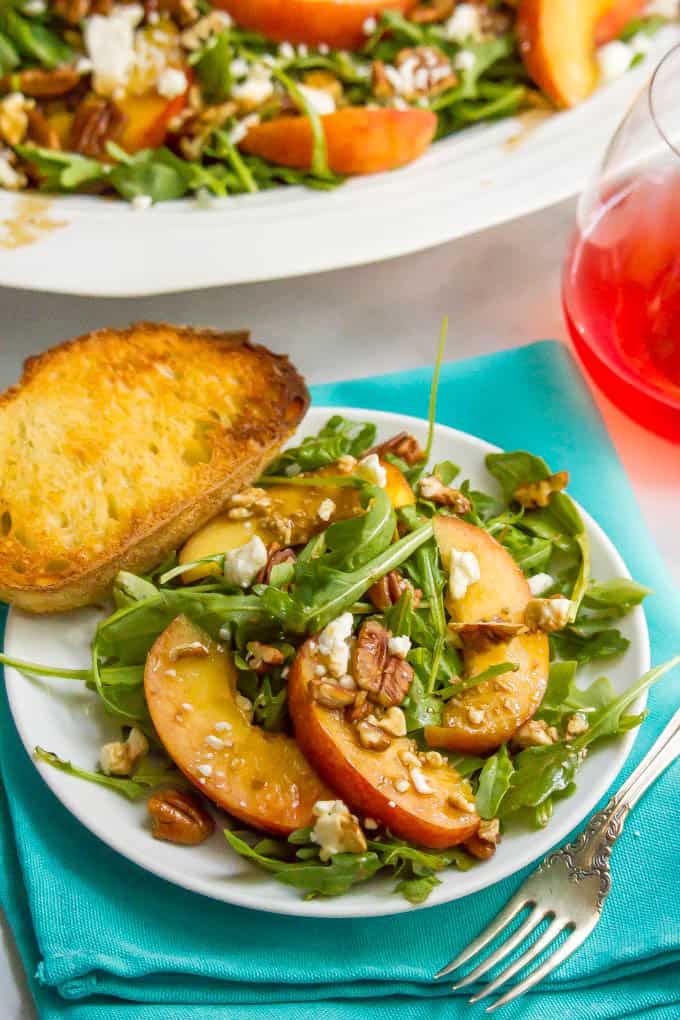 Arugula salad with peaches, pecans and goat cheese served on a white plate with crusty bread