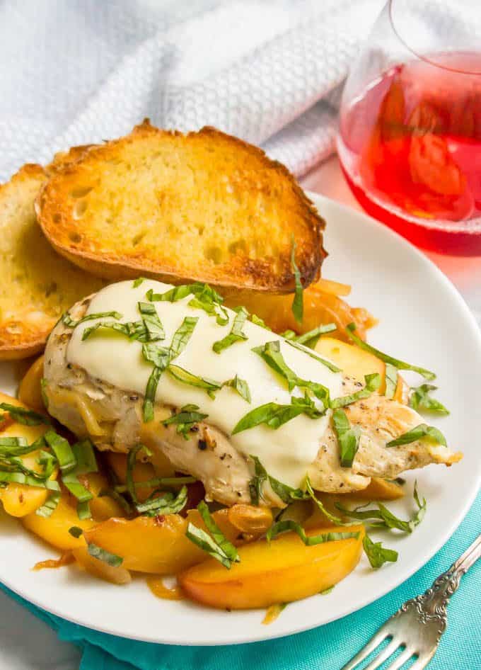 Summer skillet chicken with peaches and melted mozzarella cheese with fresh basil on top served on a plate