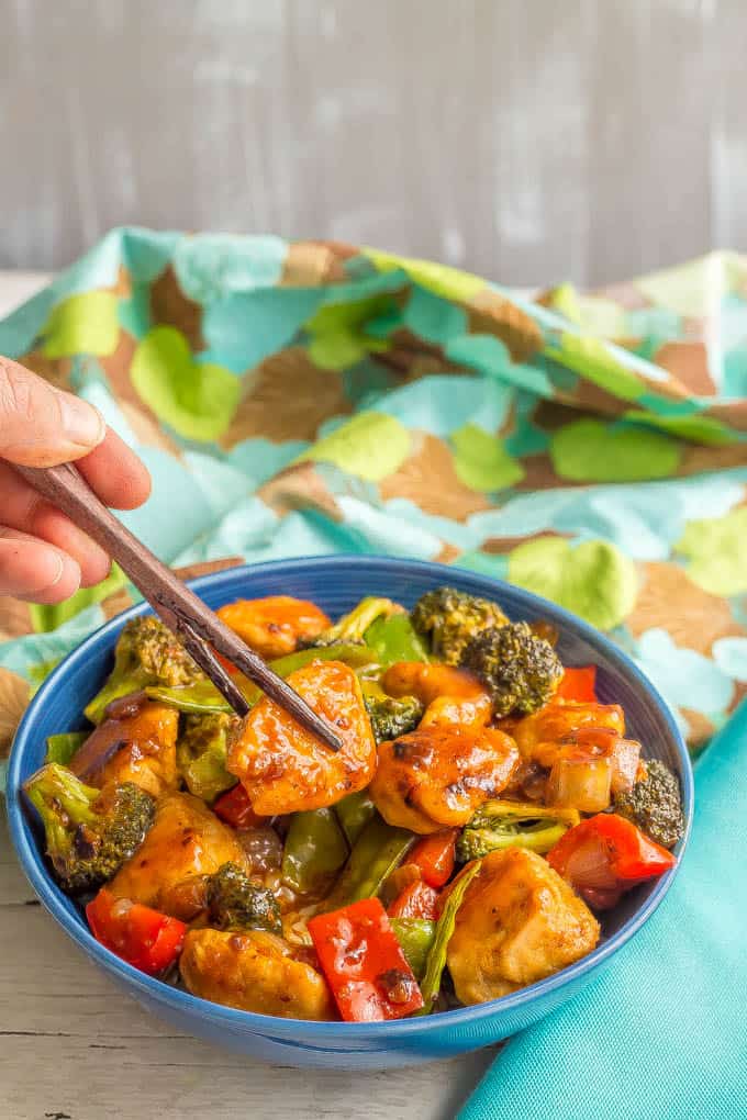 Healthy, easy sweet and sour chicken with vegetables served in a blue bowl with a bite being lifted out