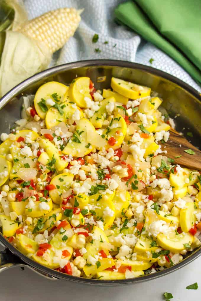 A squash and corn medley in a large deep skillet with feta cheese sprinkled on top.