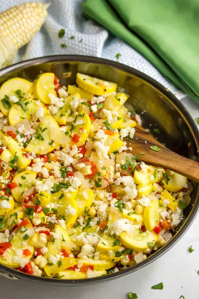 Yellow squash and corn medley in a large skillet with a wooden spoon